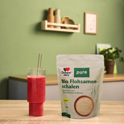 Doppelherz pure Bio Flohsamenschalen neben rotem Smoothie auf Tisch